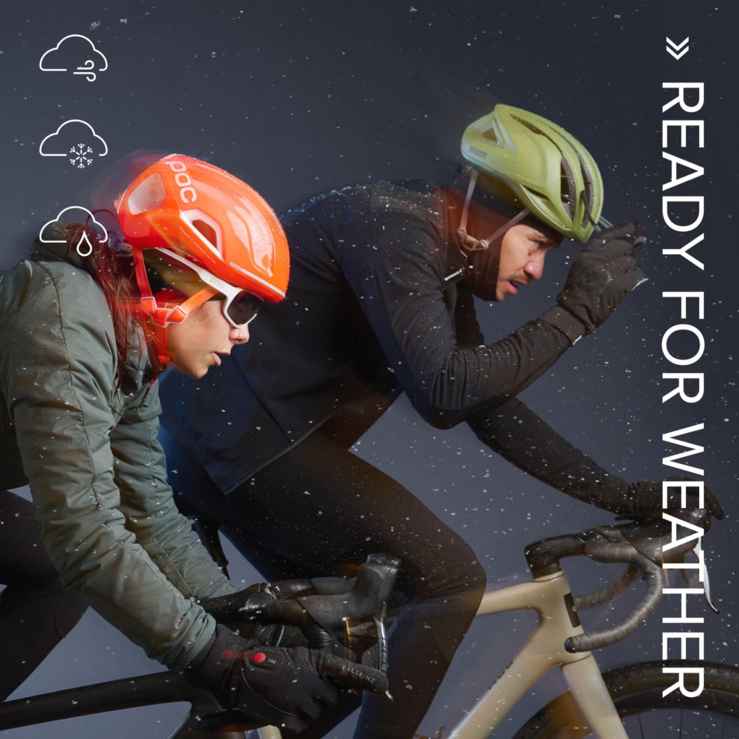 Two road cyclists in winter apparel ride in the rain. “Ready for weather” text and weather forecast icons showing wind, snow, and rain are shown on the image.
